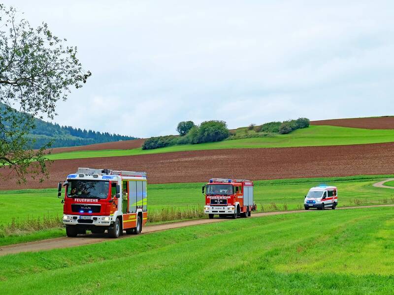 Feuerwehrfahrzeuge fahren auf einem Feldweg durch grüne Landschaft