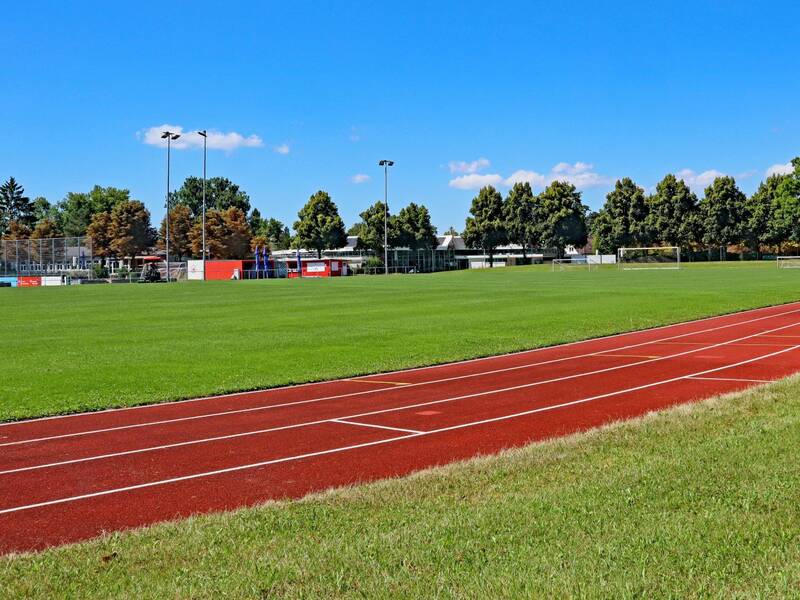 Eine Aschenbahn verläuft durch das Gras eines Sportplatzes