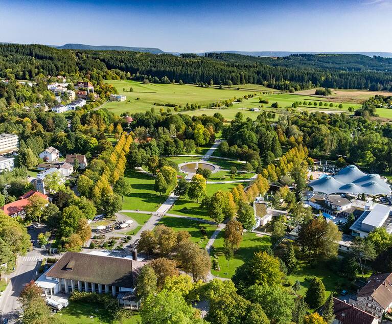 Luftaufnahme des Kurparks Bad Dürrheim mit Wegen, Wiesen, Bäumen und mehreren Gebäuden, darunter die Solemar-Therme mit Kuppeldach.