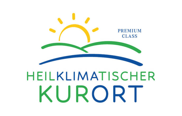 Logo mit stilisierter gelber Sonne über grünen Hügeln, darunter der Schriftzug 'HEILKLIMATISCHER KURORT' in Grün und Blau, rechts oben 'PREMIUM CLASS' in Blau.