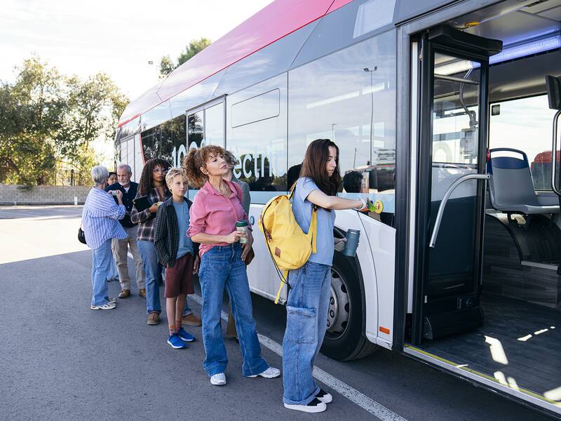 Mehrere Personen stehen in einer Reihe und steigen in einen Linienbus mit geöffneten Türen ein.