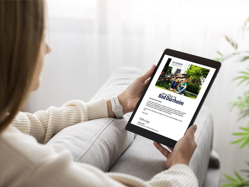 Frau sitzt auf Sofa und liest auf Tablet einen Newsletter mit Bild und Text zu Bad Dürrheim.