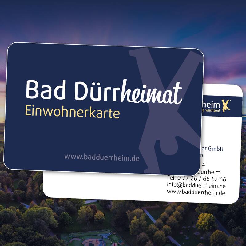 Zwei übereinanderliegende Visitenkarten mit dem Schriftzug 'Bad Dürrheim Einwohnerkarte' und Kontaktdaten vor Luftaufnahme von Bad Dürrheim im Abendlicht.