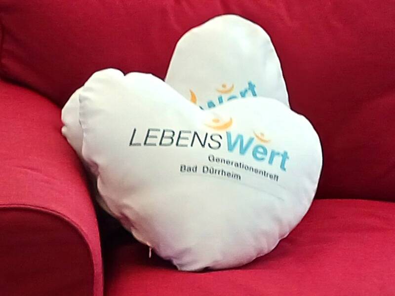 Herzförmiges Kissen mit dem Schriftzug 'LEBENSWert Generationenzentrum Bad Dürrheim' auf rotem Sofa