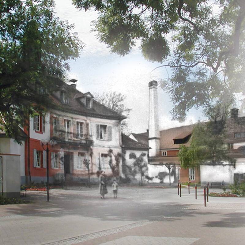 Blick auf einen Platz mit Bäumen, einem historischen Gebäude und einer alten Fabrik mit Schornstein, teils in Farbe, teils in Schwarz-weiß.