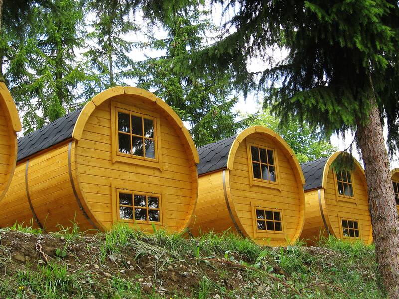 Vier runde, gelb gestrichene Holzhäuser in Fassform stehen in einer Reihe im Wald.