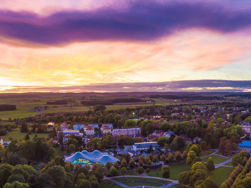 Luftaufnahme eines Parks mit Wegen, Bäumen und Gebäuden bei Dämmerung unter einem farbigen Himmel