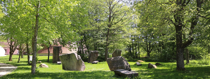 Grüner Park mit mehreren großen, unregelmäßig geformten Steinen, die in einem lockeren Kreis angeordnet sind, umgeben von Bäumen.