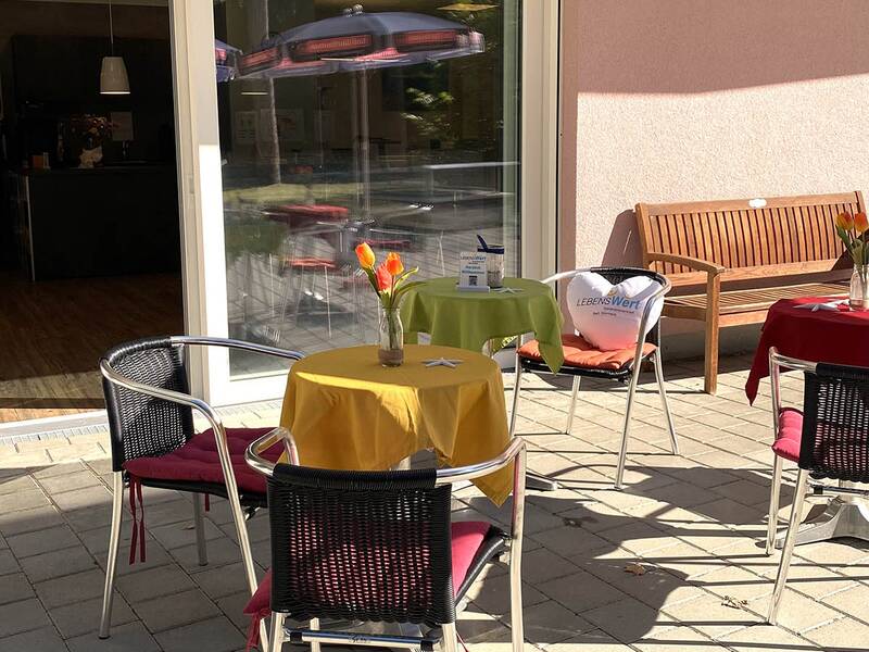 Terrasse mit mehreren Tischen und Stühlen vor einem Gebäude mit großer Glasschiebetür