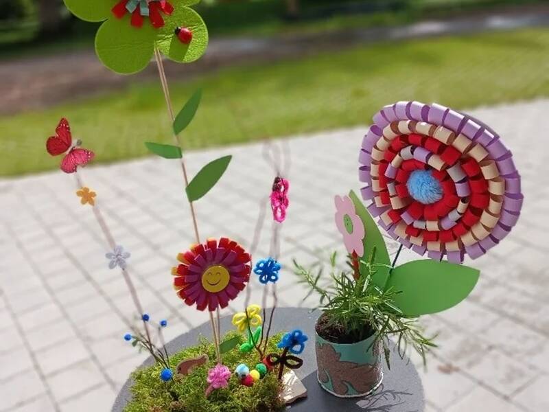 Bunte Bastelblumen aus Papier und Holz auf einem kleinen runden Tisch im Freien