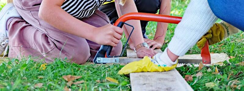 Drei Kinder arbeiten mit Werkzeug und Handschuhen an einem Holzbrett