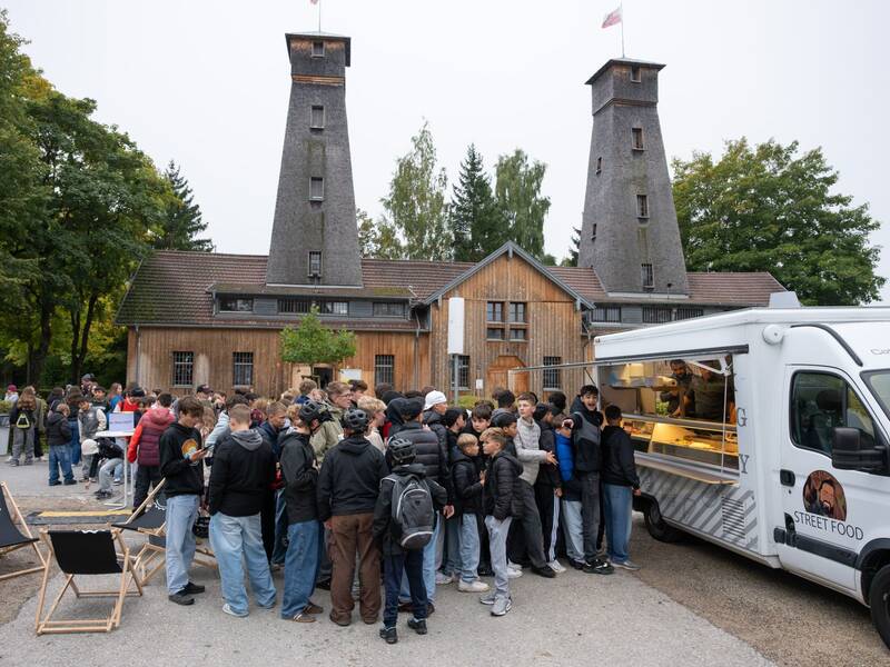 Eine Gruppe von Menschen vor einem Street Food-Auto. Im Hintergrund zwei Türme mit Flaggen auf der Spitze.