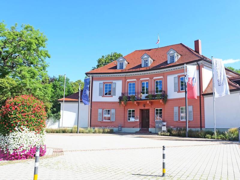 großes Gebäude mit vielen Fenstern und bepflanztem Balkon auf einem großen Platz