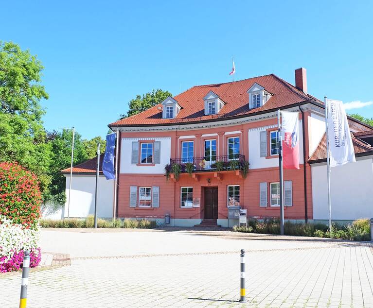 großes Gebäude mit vielen Fenstern und bepflanztem Balkon auf einem großen Platz