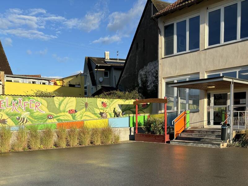 Außenansicht der Einrichtung mit Eingangstür und bunt bemalter Nachbarsmauer