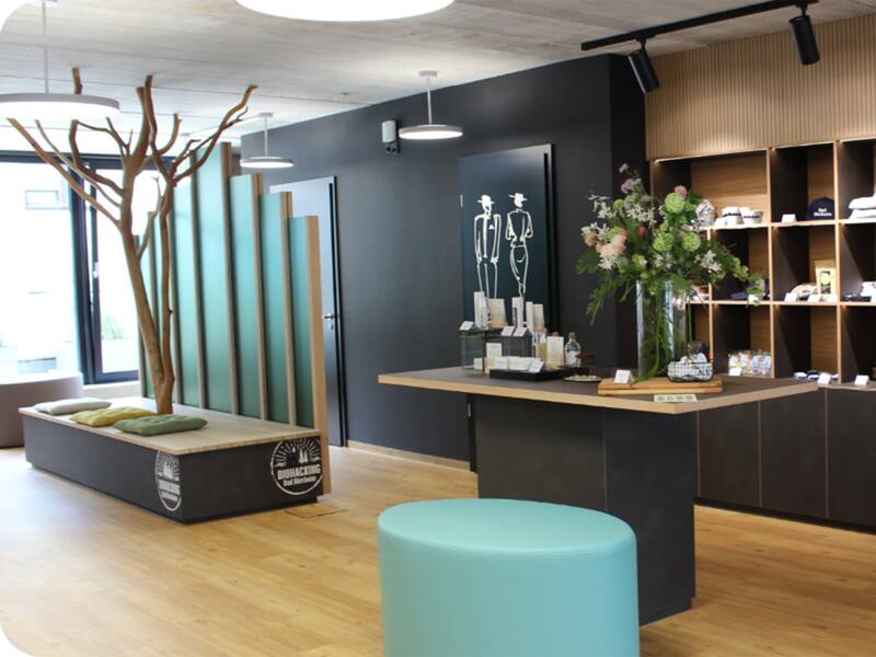 Moderner Innenraum einer Touristinfo mit Sitzbank, Stehtisch, Blumenarrangement und Souvenirs an der Wand