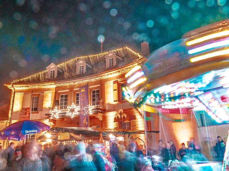 Weihnachtlich beleuchtetes historisches Gebäude mit Menschenmenge und unscharfem Karussell in Bewegung bei Nacht
