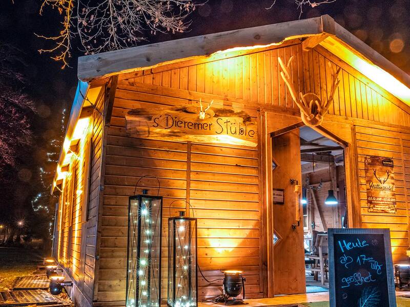 Beleuchtete Holzhütte mit Schildern und Tafel vor dem Eingang in einem Park bei Nacht