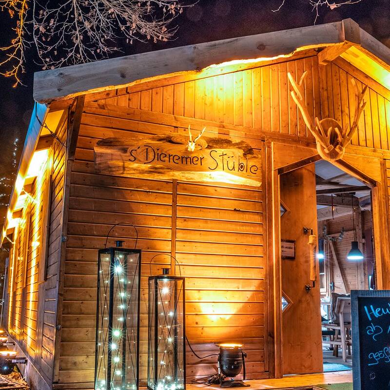 Beleuchtete Holzhütte mit Schildern und Tafel vor dem Eingang in einem Park bei Nacht