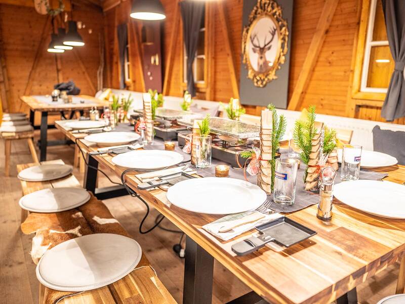 Langer Holztisch in einer Hütte mit gedeckten Plätzen, Gläsern, Besteck und kleinen Tannenzweigen als Dekoration