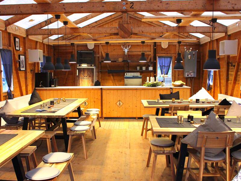 Rustikale Holzhütte mit Tischen, Bänken, Stühlen und Kücheneinrichtung in warmem Licht