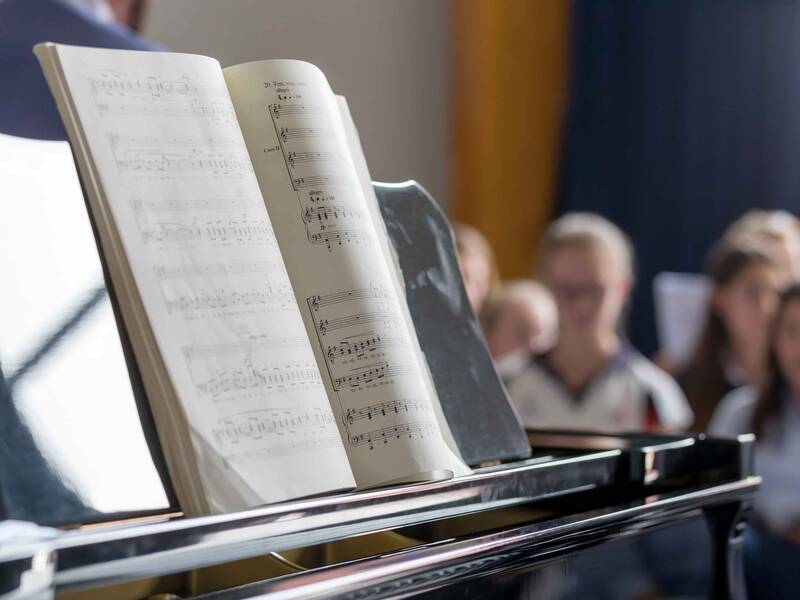 Schwarzes Klavier mit Notenblättern, Im Hintergrund sind singende Persoenen.