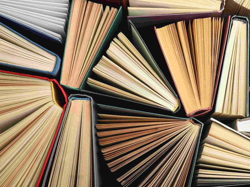 Mehrere aufgeschlagene Bücher liegen eng nebeneinander mit sichtbaren Buchrücken und Seitenkanten.