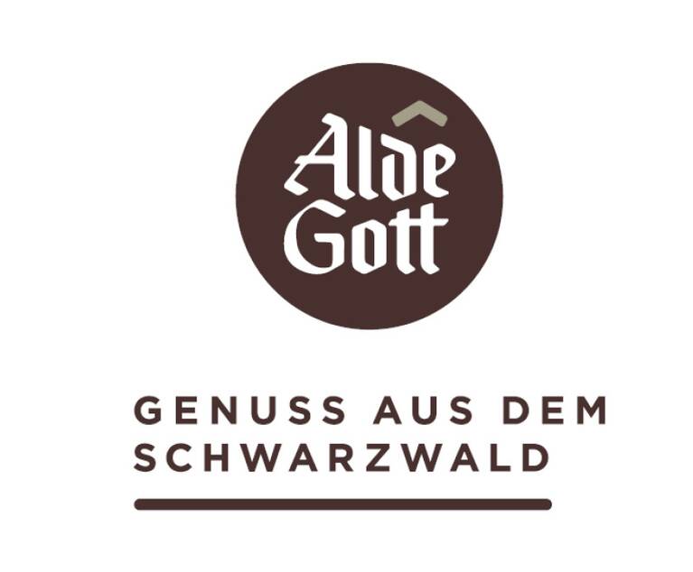 Braunes rundes Logo mit weißer Schrift 'Alde Gott' und darüber kleinem stilisiertem Dach, darunter der Text 'GENUSS AUS DEM SCHWARZWALD' in Großbuchstaben mit Unterstreichung