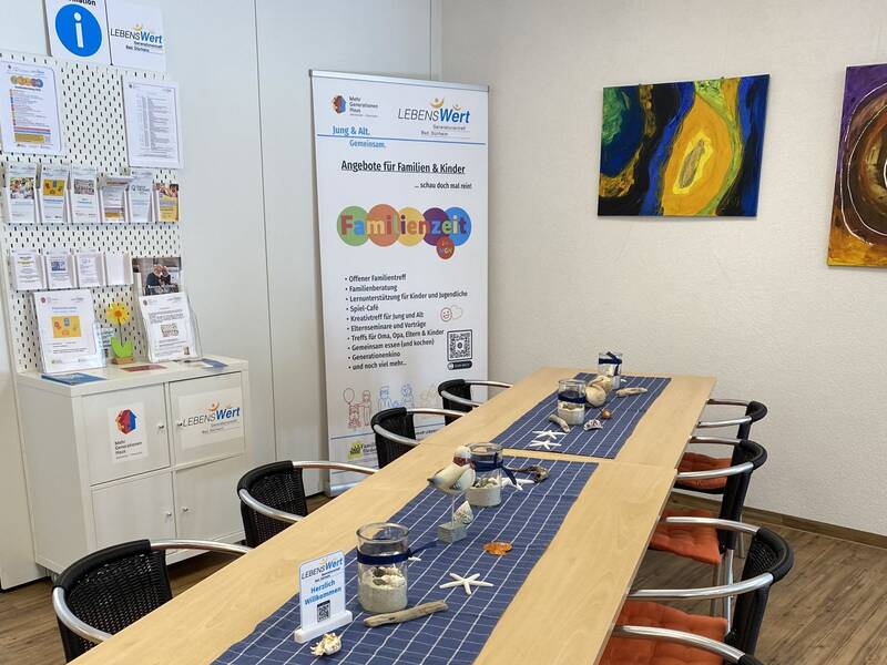 Langer Tisch mit Stühlen und dahinter ein Regal mit Informationsmaterial